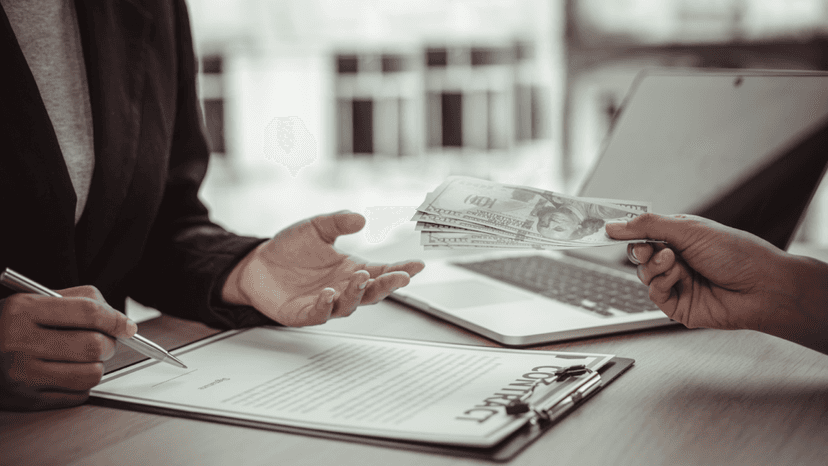 Business agreement being signed while money is exchanged between two people at a desk.
